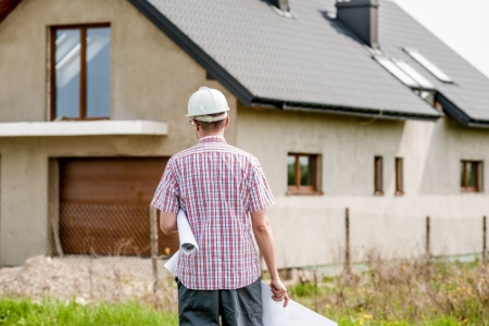 Homme de dos portant un casque de chantier près d'une maison en cours de rénovation