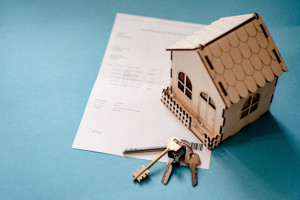 Clé de maison posée sur un contrat avec une maquette de maison en bois.