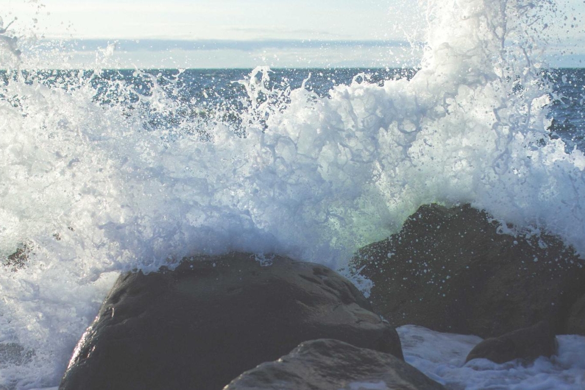 Waves crash against dark rocks along a rocky shoreline, sending white spray into the air.
