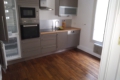 Blurry modern kitchen with stainless steel appliances, wooden floor, and a sink along the counter.