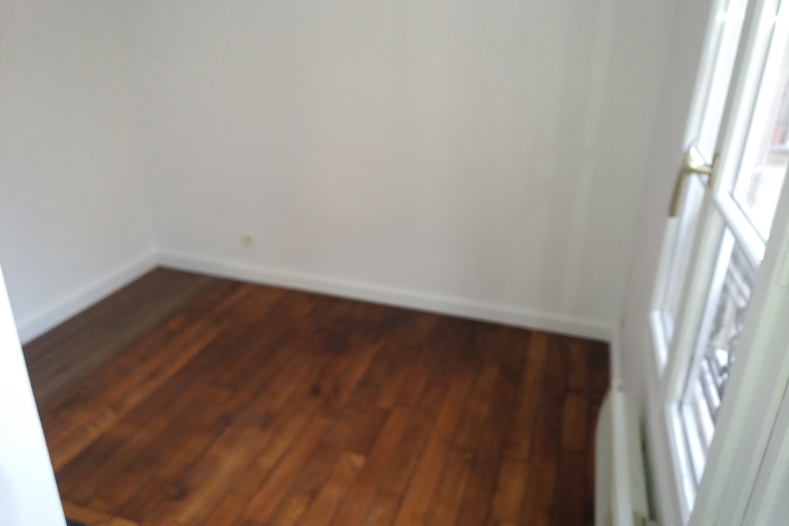 Corner of a small room with dark wood flooring, white walls, baseboard trim, and a glass door with panes on the right side.