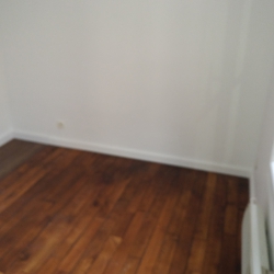 Corner of a small room with dark wood flooring, white walls, baseboard trim, and a glass door with panes on the right side.