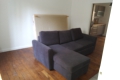 Blurry living room with a dark blue sectional sofa, light walls, and a doorway to a kitchen area in the background.