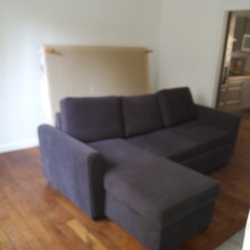 Blurry living room with a dark blue sectional sofa, light walls, and a doorway to a kitchen area in the background.
