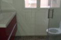 Blurry bathroom scene with a white toilet on the right, a sink countertop on the left, and a door with a window leading to a light-filled building exterior visible in the background.