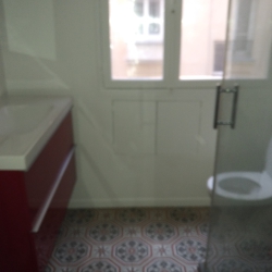 Blurry bathroom scene with a white toilet on the right, a sink countertop on the left, and a door with a window leading to a light-filled building exterior visible in the background.