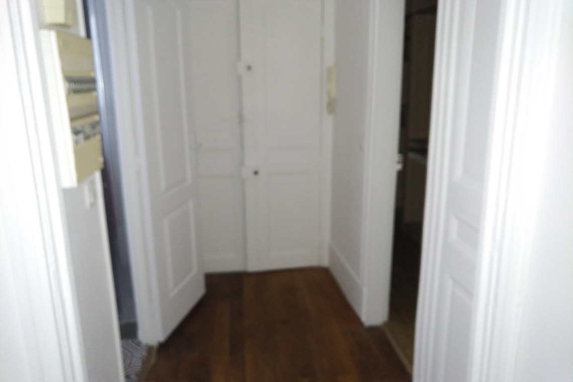 Blurry view down a narrow hallway with white-paneled doors on both sides and a wooden floor, seen from eye level.
