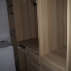 Blurred view of an open wooden wardrobe with built-in shelves; a washing machine is visible on the left side.