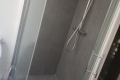 Glass-walled shower enclosure with dark gray tiled walls, a handheld shower head on a vertical bar, and a square floor drain.