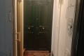 Narrow hallway with a warm wooden floor leading to a dark green double front door with ornate molding above, and a beige door on the left side.