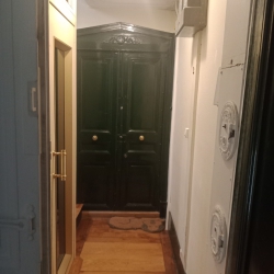 Narrow hallway with a warm wooden floor leading to a dark green double front door with ornate molding above, and a beige door on the left side.