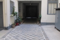 Narrow white-walled alley with a patterned stone floor and potted plants along the left wall, leading to a dark entrance corridor.